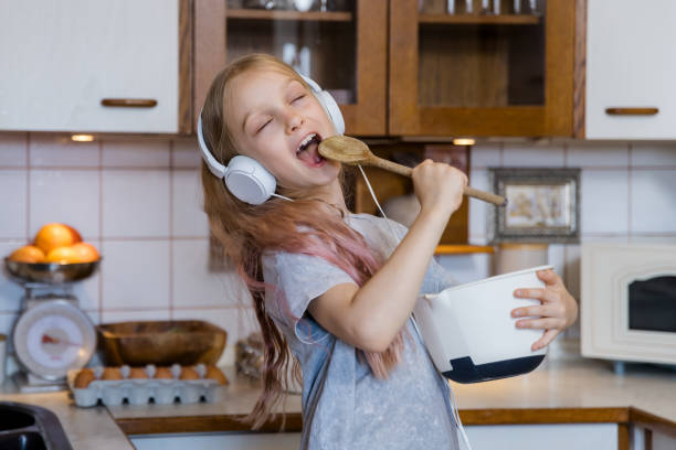 Little girl listeing music in headphones and preparing food in kitchen