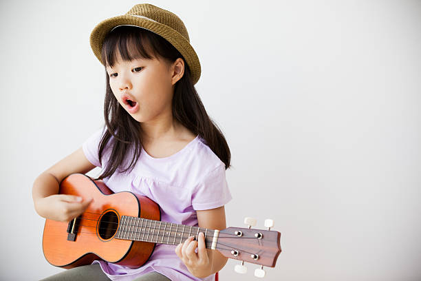 Little Chinese girl singing and playing ukulele.